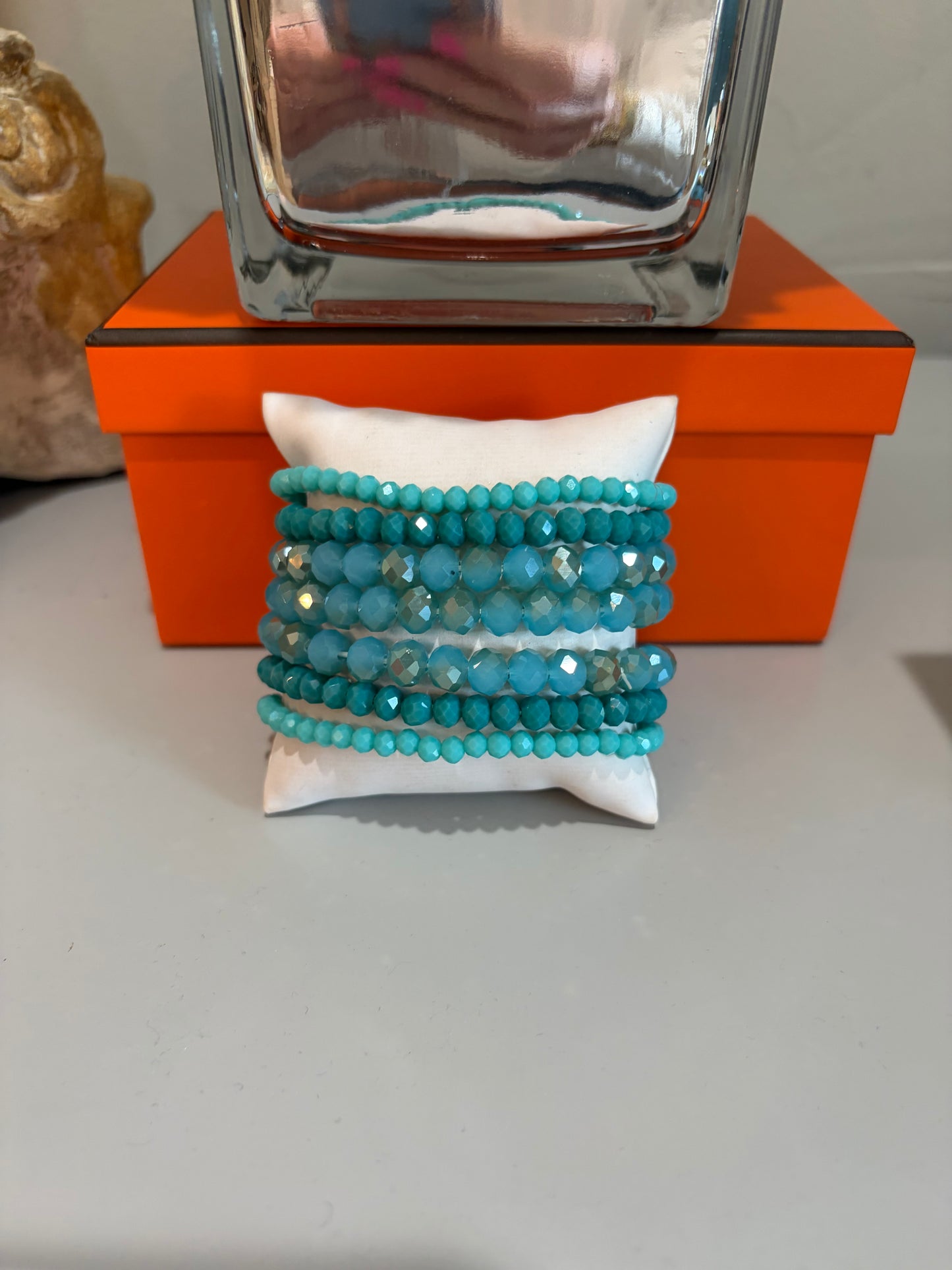 Turquoise beaded bracelets on a white pillow with an orange box in the background
