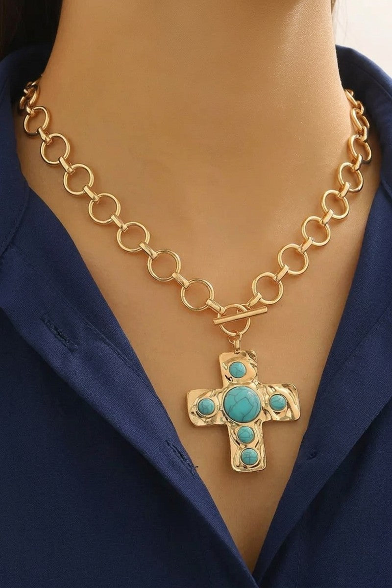 Gold chain necklace with a turquoise cross pendant on a person wearing a navy blue outfit.