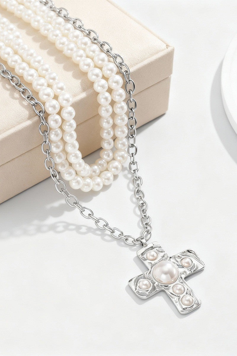 Pearl necklace with a silver cross pendant on a white surface