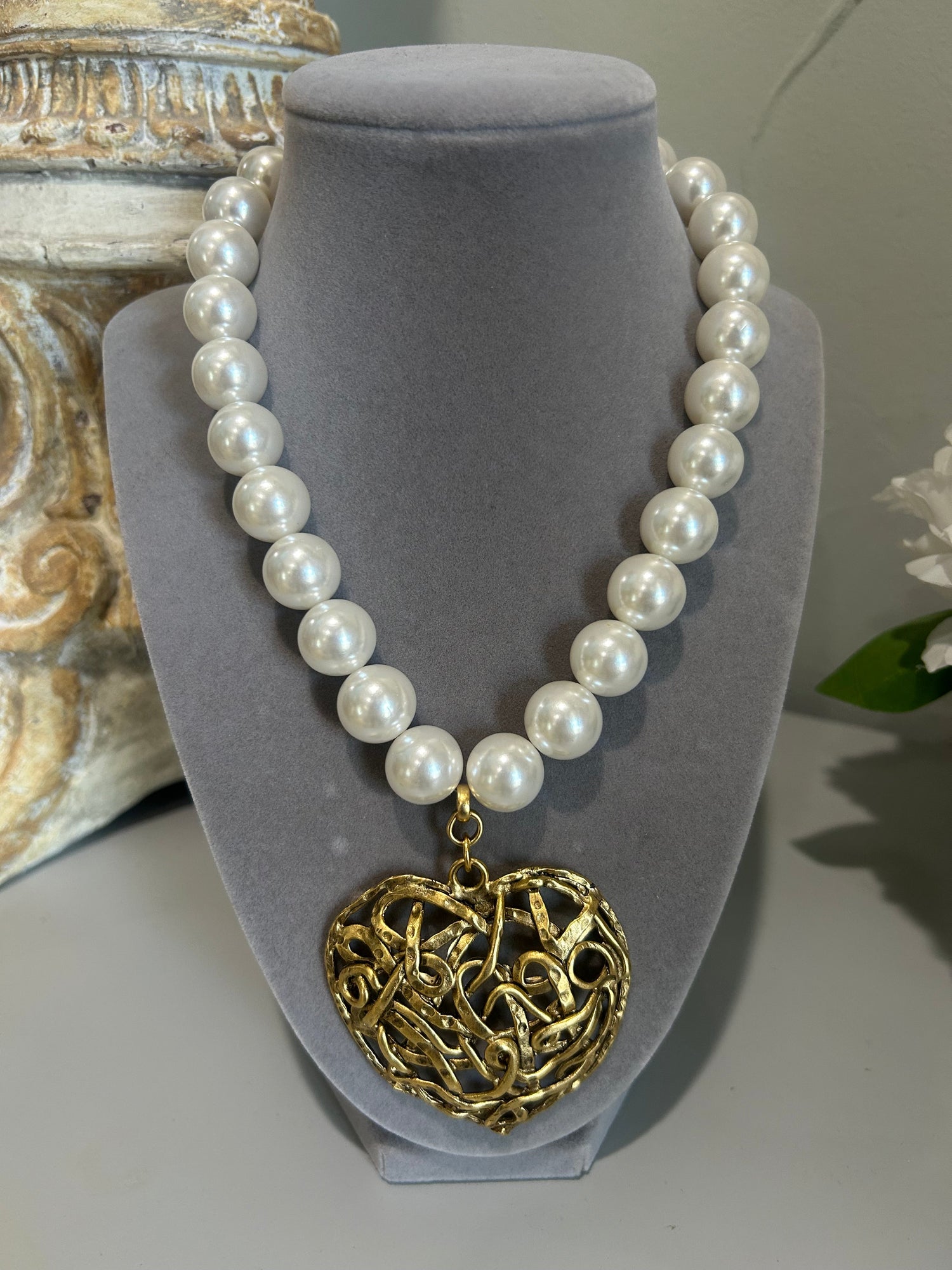 Pearl necklace with a gold heart-shaped pendant on a gray stand.