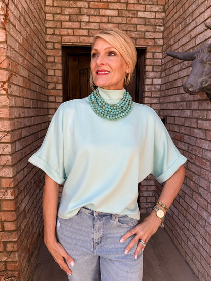 woman wearing a sea foam green pullover with a mock neck, short sleeve. 