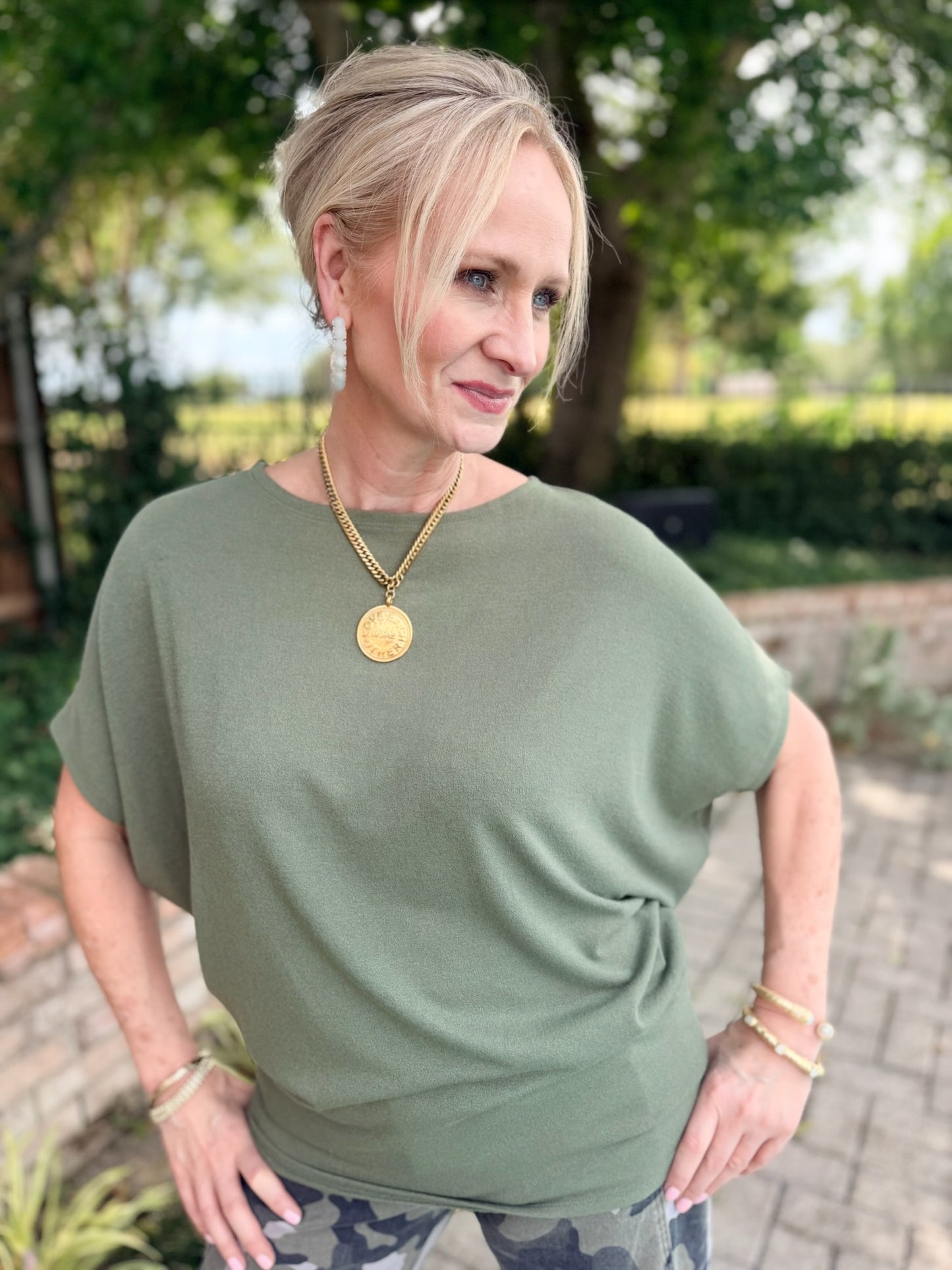 An olive green dolman style, short sleeve top.  Paired with gold medallion necklace and camo bottoms.