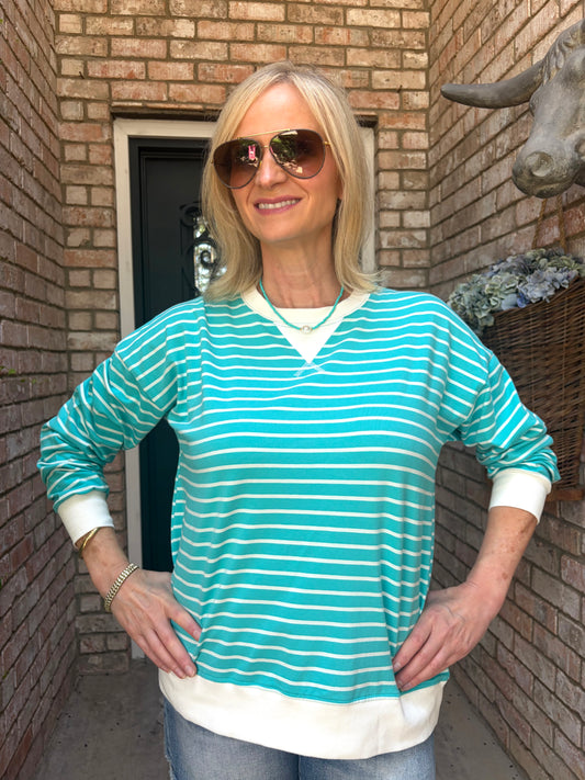 woman wearing a turquoise pullover with white stripes, white around the wrists, neck and waist band of top 