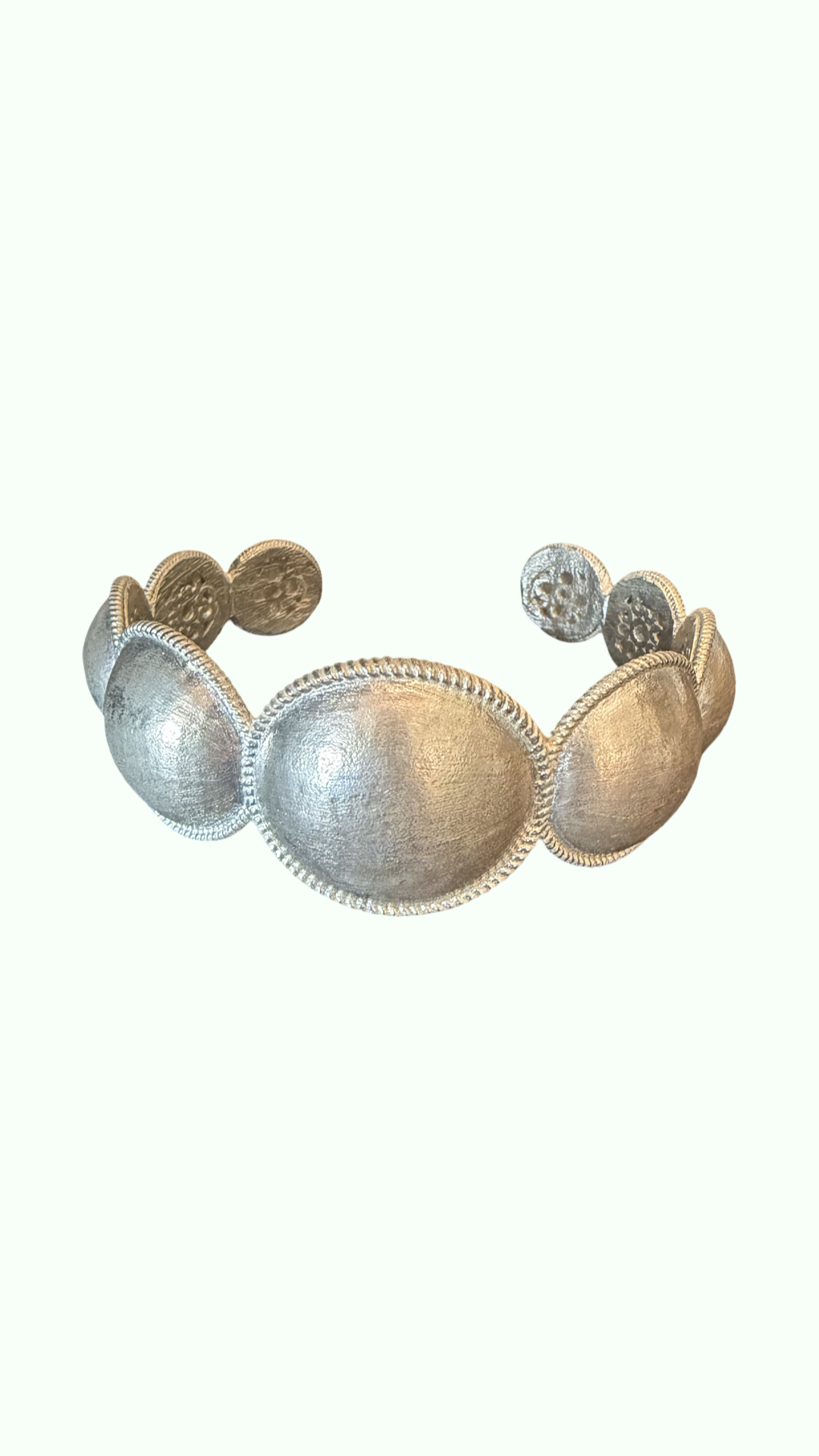 A silver-toned metal cuff bracelet featuring a series of textured, dome-shaped segments with decorative beaded borders, set against a solid off-white background.