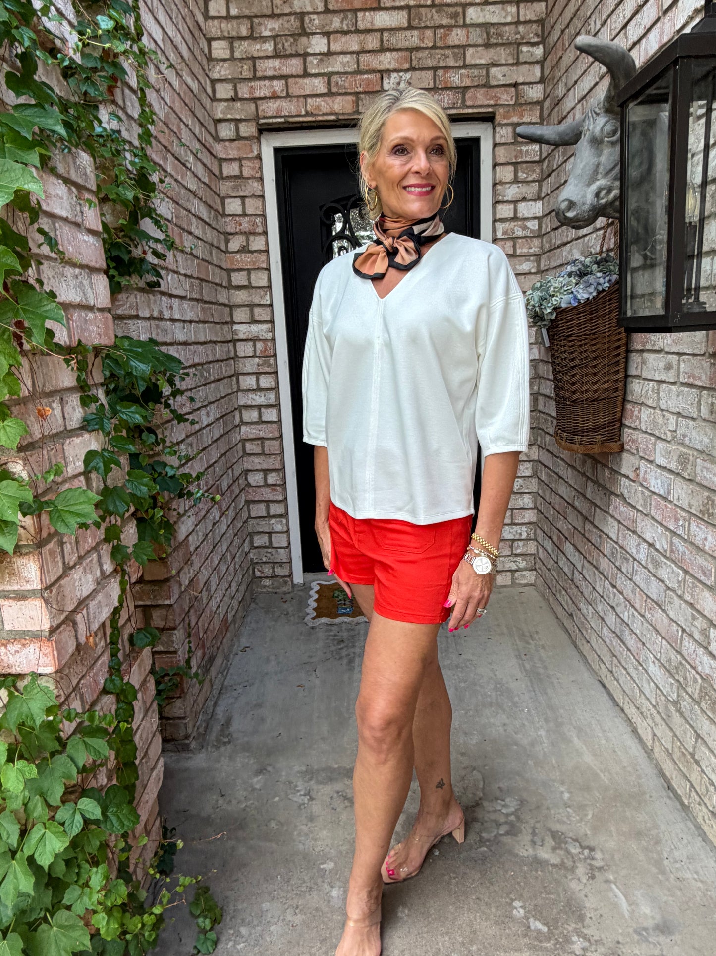 Person wearing a white shirt and red shorts standing on a brick path with plants around.