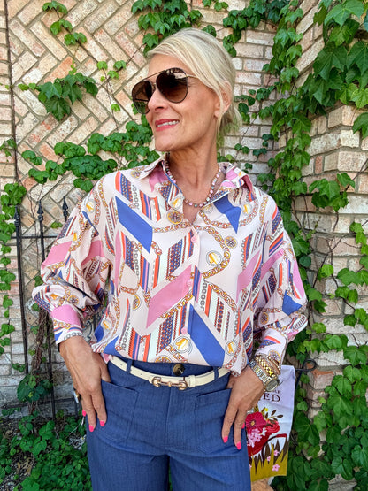 Woman wearing a patterned blouse, button down, long sleeve, blues and pinks, orange paired with a blue pant with front pockets, flair leg
