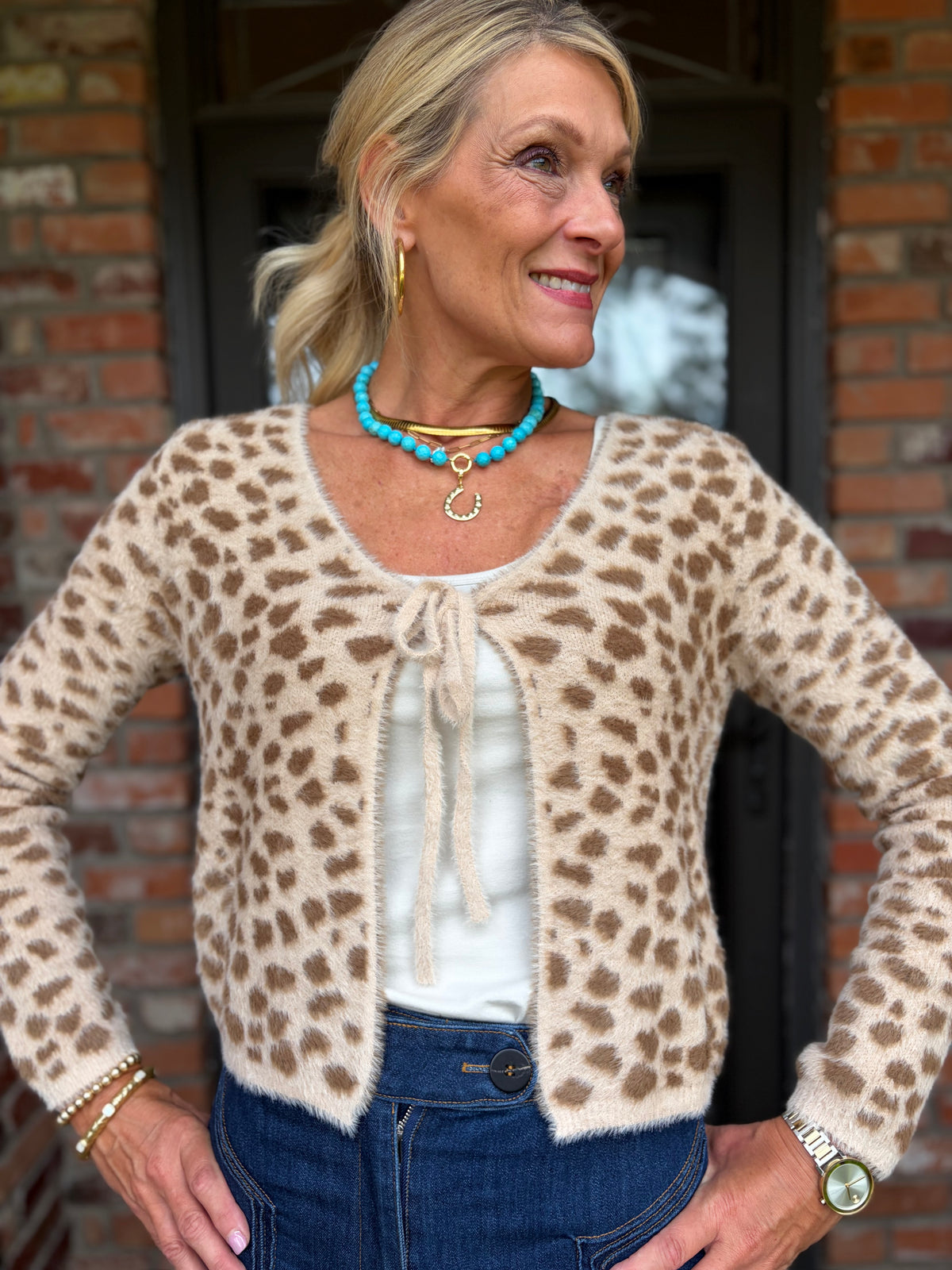 A woman wearing a fuzz, beige and tan  leopard-print cardigan that is long sleeved and ties in front 