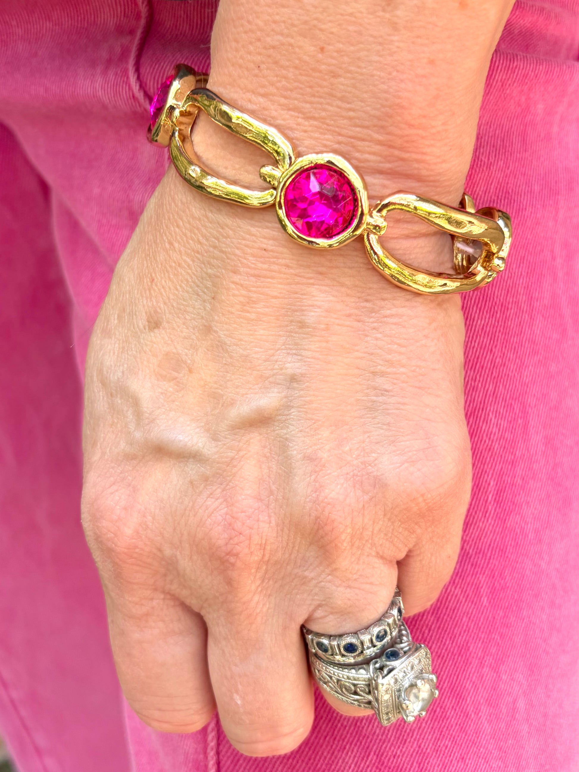a hammered gold modern link bracelet that is stretch with alternating round, bright pink crystals.
