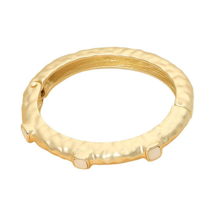 A gold-plated bangle bracelet with a textured, hammered finish and small white rectangular inlays at the front, shown on a plain white background.