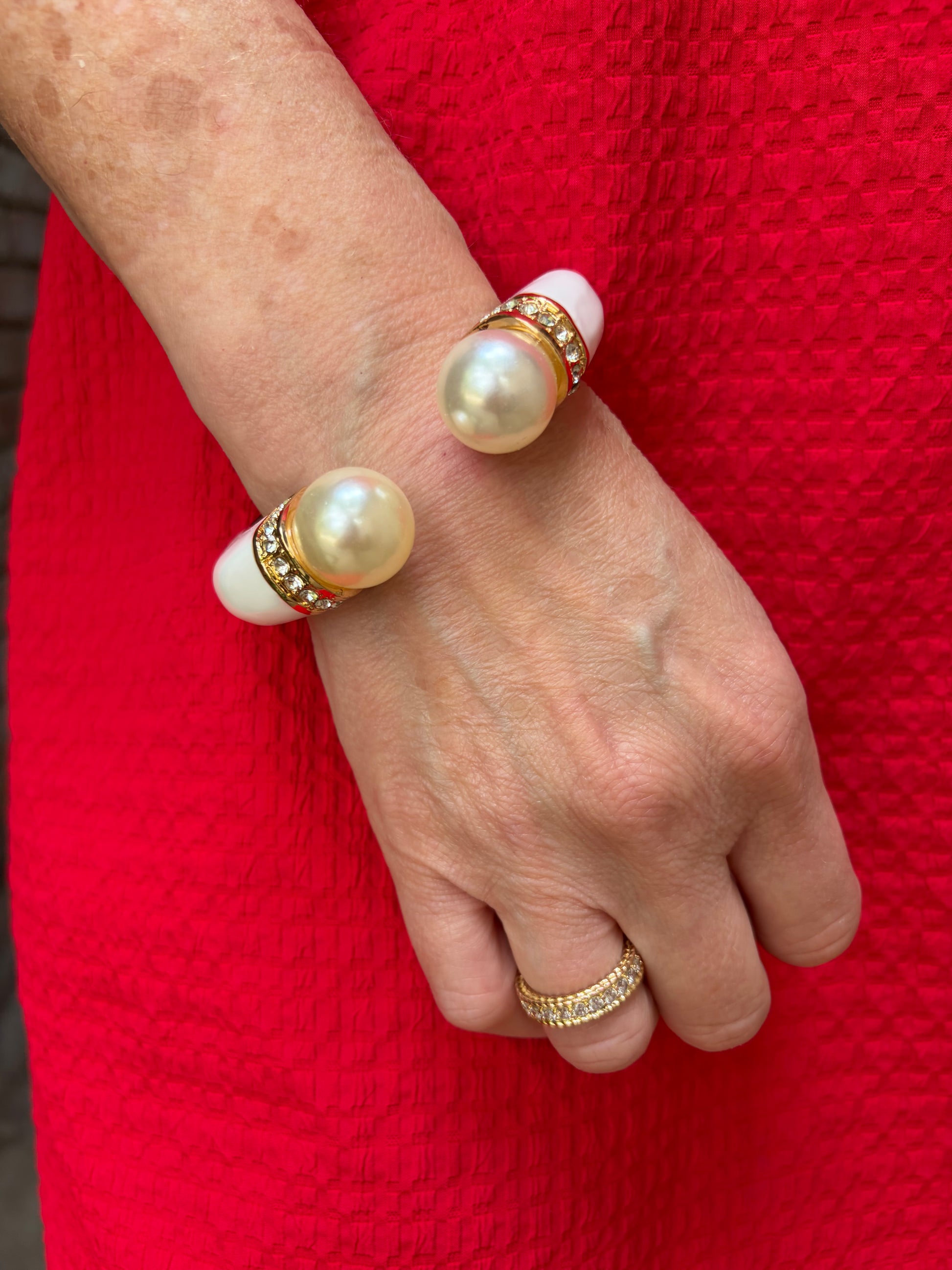 Hand wearing a pearl bracelet and ring against a red background