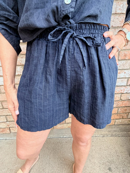 Lady wearing navy blue linen pin stripe mid length drawstring shorts with a tie. 