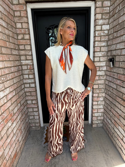 woman in off white summer knit sweater, linen zebra pants and an orange horsebit scarf