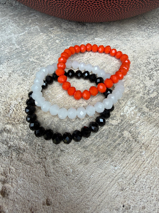 Three beaded stretch bracelets in orange, translucent white, and glossy black