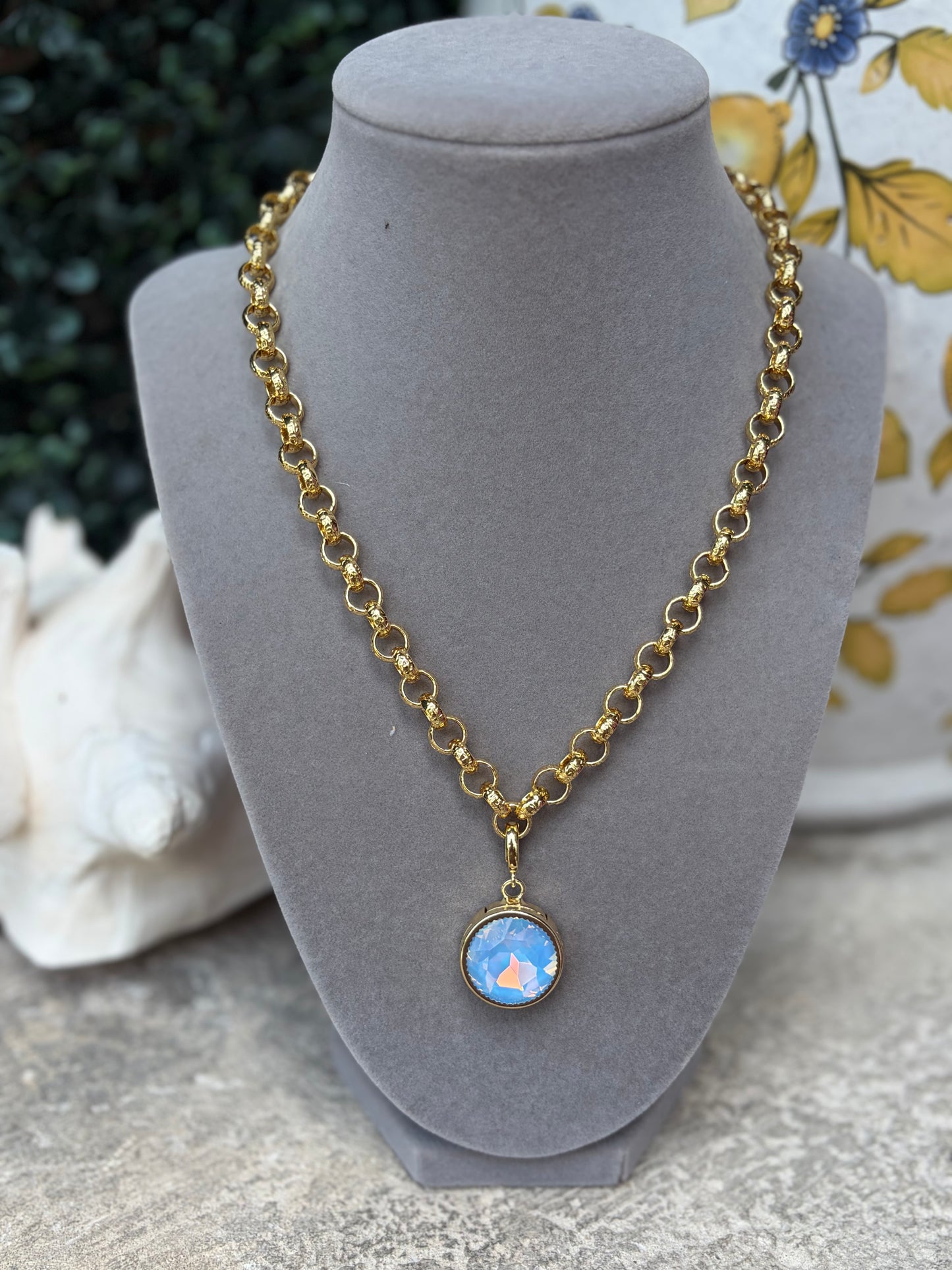 A round light blue gemstone charm on a link gold necklace