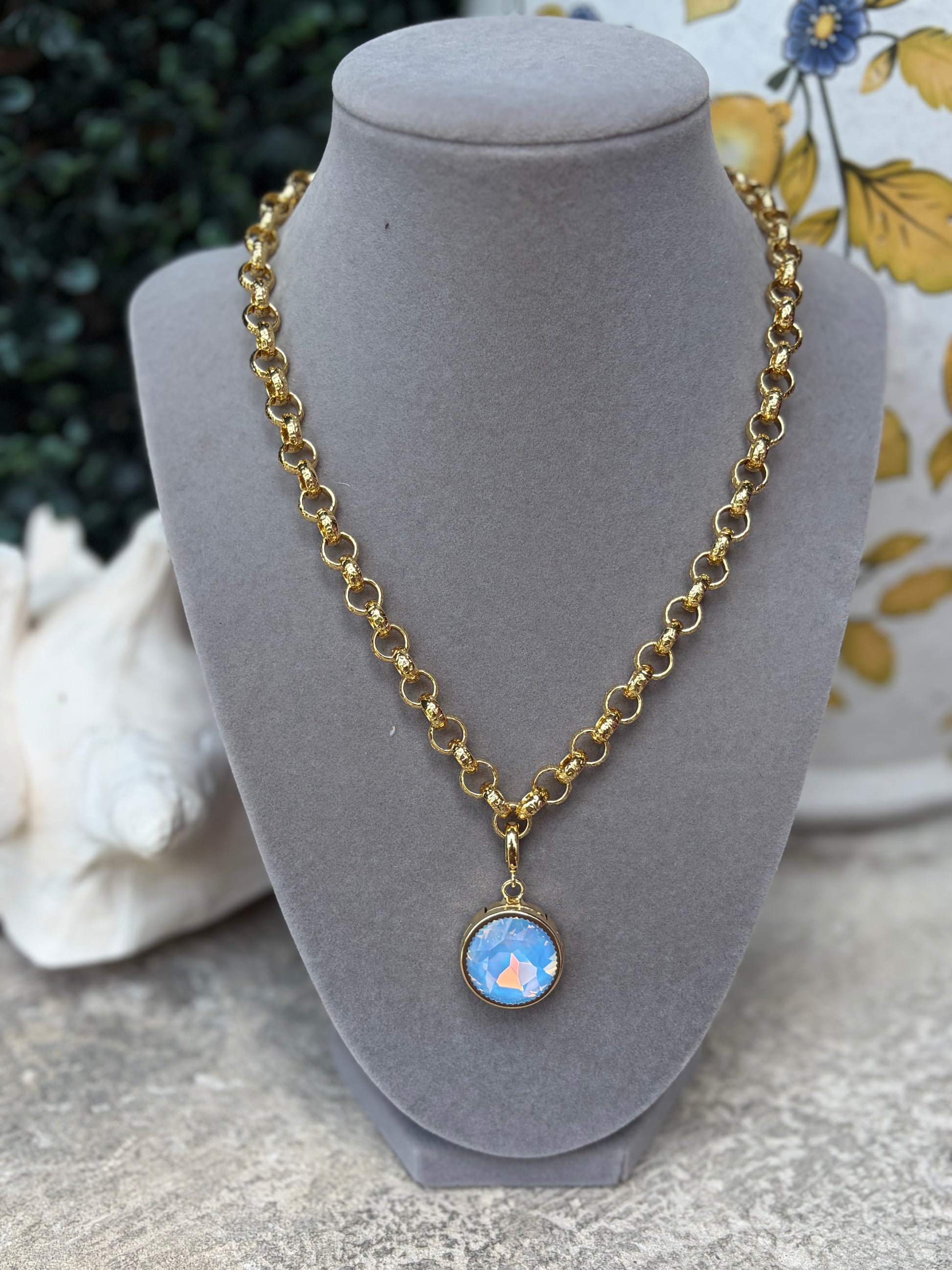 A round light blue gemstone charm on a link gold necklace