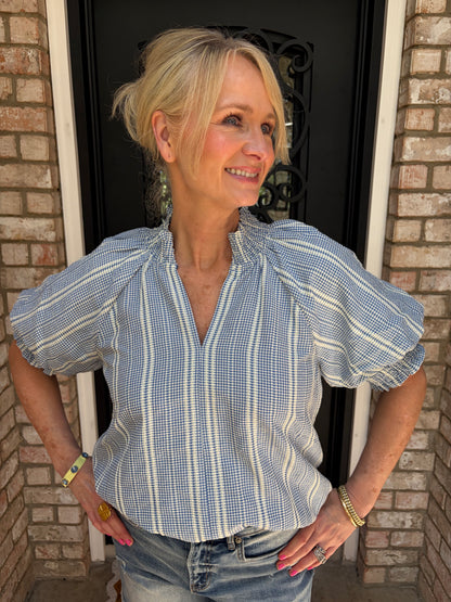 Woman wearing a blue and white striped shirt, v neck, puff sleeve, paired with frayed hem denim shorts