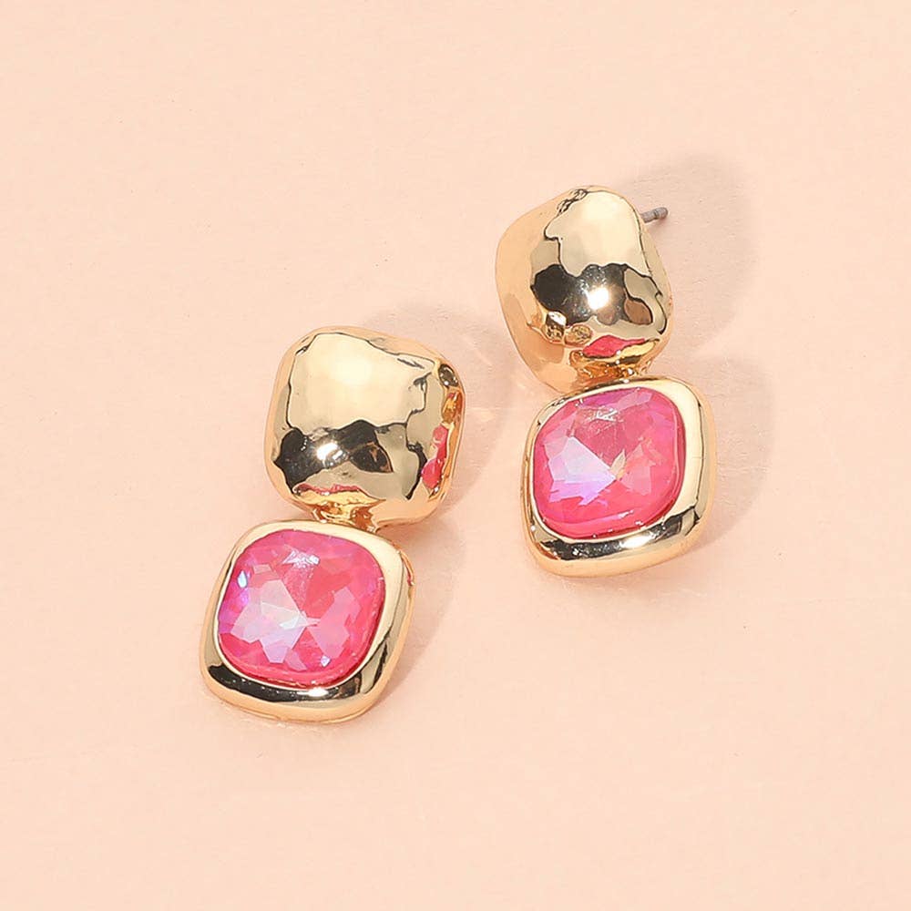 A pair of gold-toned drop earrings with a textured metallic top and a square pink faceted gemstone setting below, displayed on a solid pale pink background.