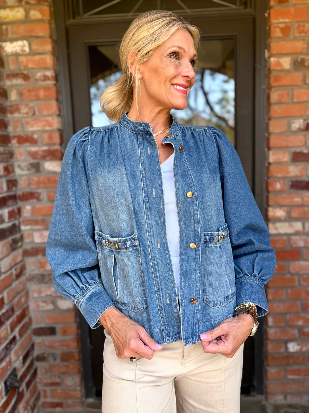 lighter blue denim jacket/blazer that is faux, crew neck with gold buttons, gold horse bit detail on the front pockets with puff sleeve and cuff detail. 