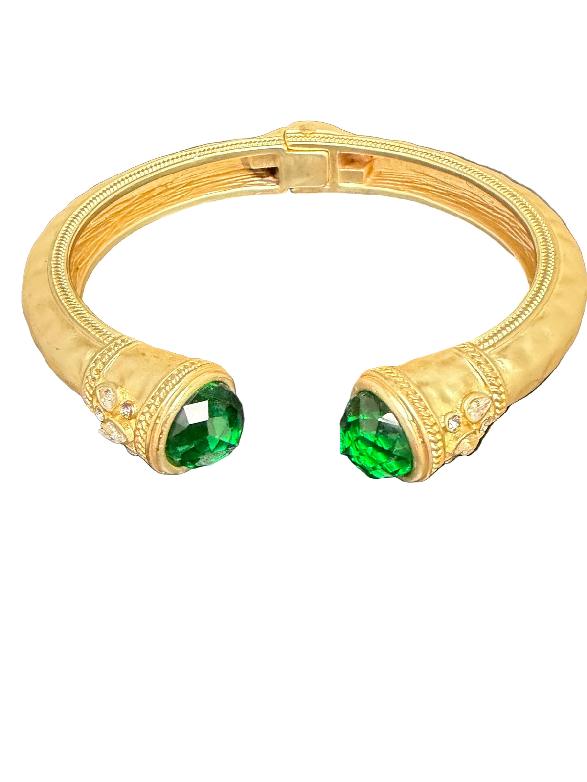 A gold-toned cuff bracelet with two large oval green gemstones and small clear stones, photographed on a dark textured surface.