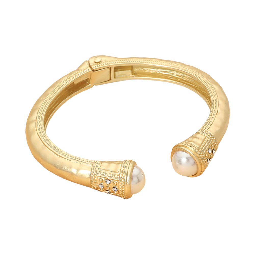 A gold-toned open cuff bracelet featuring round white pearl accents at each end, decorated with small clear rhinestones, shown on a plain white background.