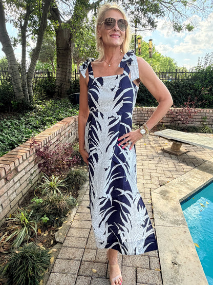woman in a blue and white botanical print dress with ties at the shoulder, zipper on the side, side slit and built in slip