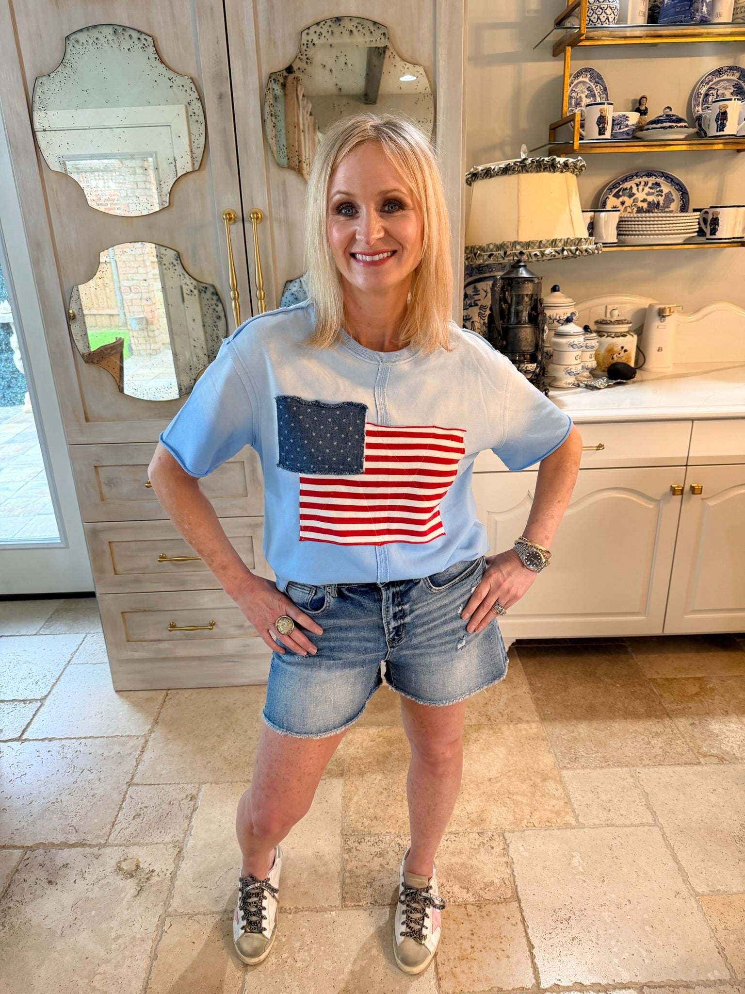 woman wearing blue tee with american flag design and expose seams and denim shorts
