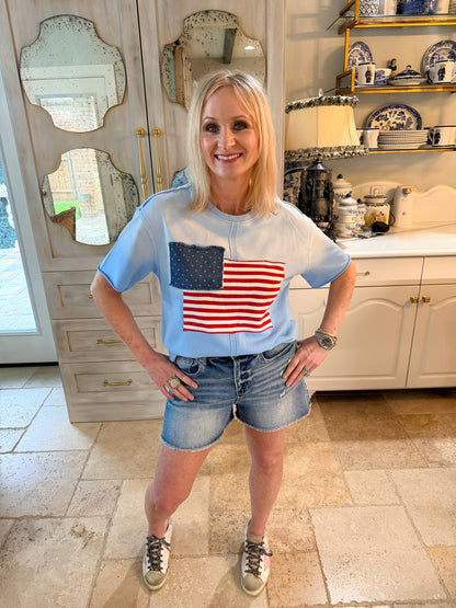 woman wearing blue tee with american flag design and expose seams and denim shorts
