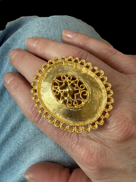 Gold ring with intricate design held by a hand against a blurred background