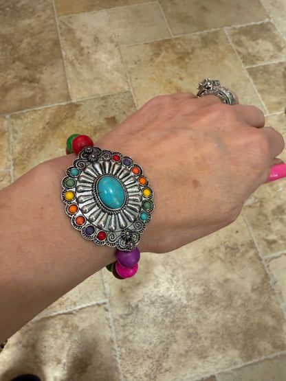 silver concho bracelet with turquoise center stone and smaller stones in color around it. Colorful beads that make up the stretch band