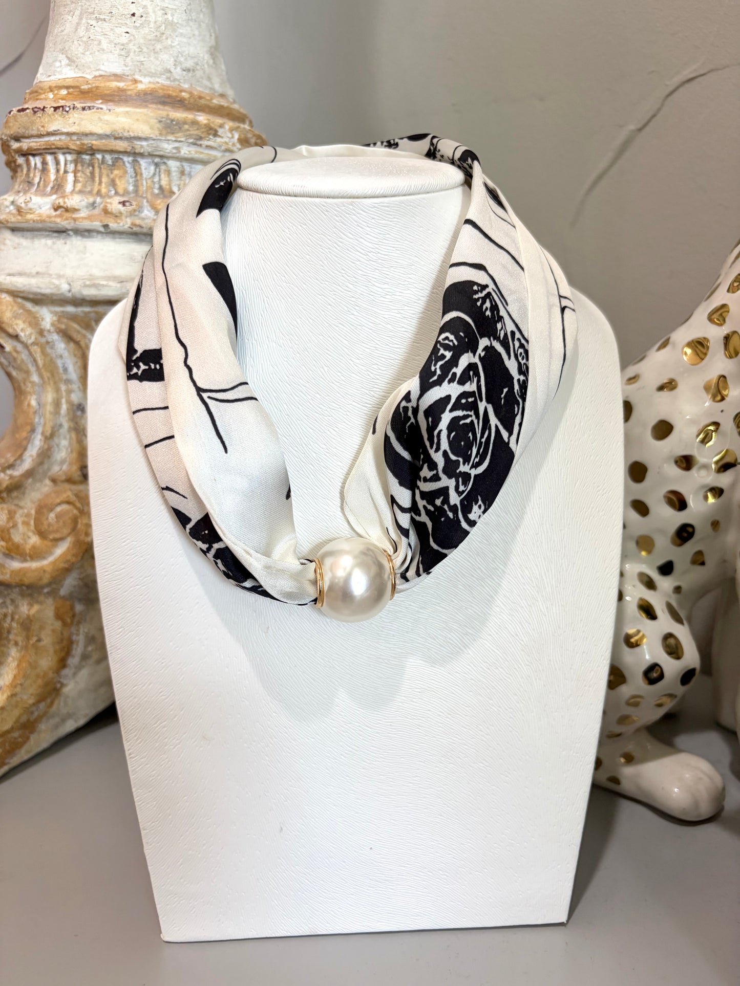 A black and white patterned scarf with a large white pearl pendant, displayed on a white mannequin bust.