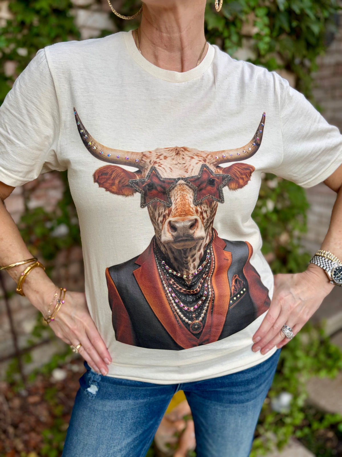 a woman in cream tee with a longhorn graphic with star sunglasses, rhinestone accents and in an orange and black jacket