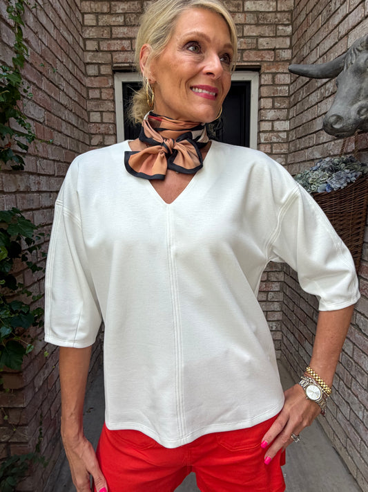 woman in an off white butter soft stretch v neck top with beige plaid scarf around her neck and red shorts

