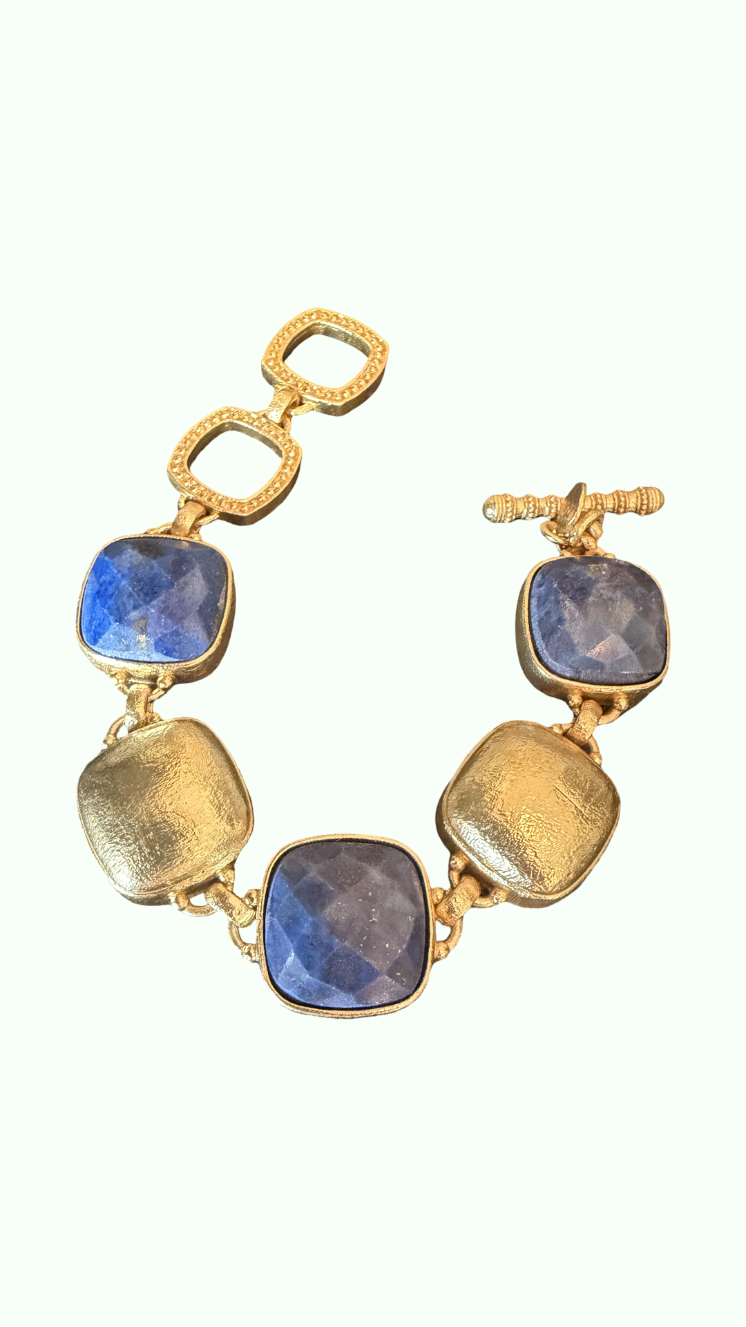 A gold-tone chain bracelet featuring three large, polished blue gemstones and three textured gold square links, displayed on a clean off-white background.