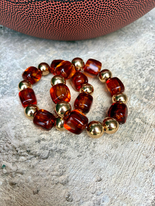A beaded stretch bracelet made of translucent amber-brown  beads and shiny gold metallic beads