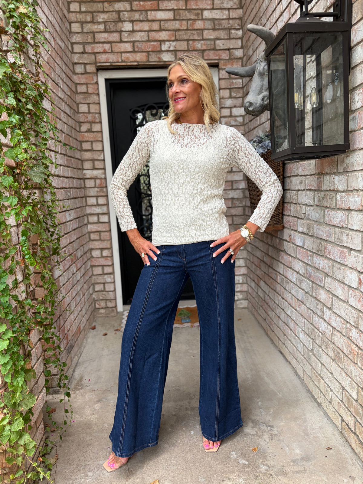 a light beige round neck lace top with long sleeves. Layered over a light colored tank top with dark denim jeans
