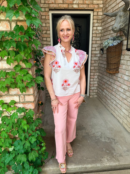 Woman in a white blouse with floral patterns, flutter sleeve, v neck and pink pants.