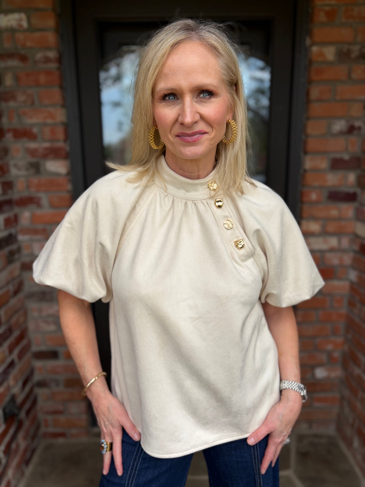 a cream colored thml round mock neck suede like blouse with half, short sleeve that is aline fit with 4 gold hammered buttons up the front at an angle  at neck line