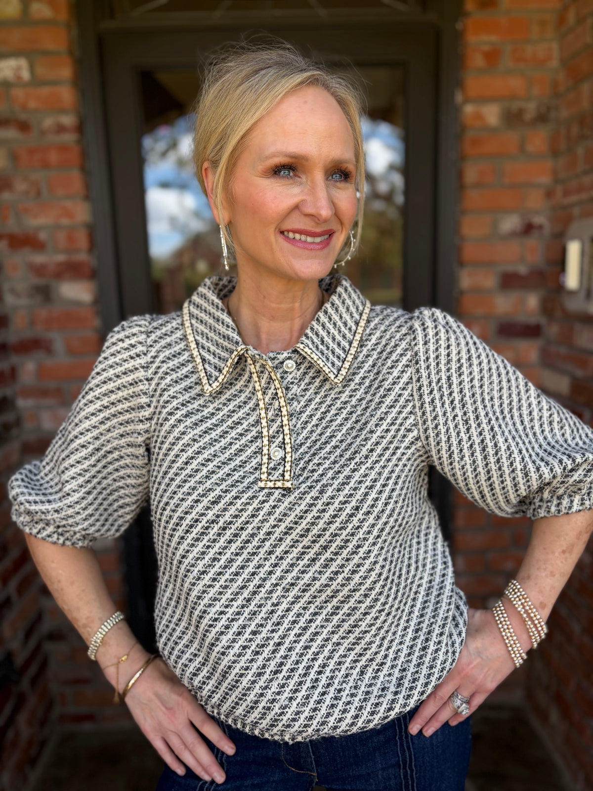 A grey and white textured tweed blouse that is short sleeved with gold threading details and v neck with pearl buttons 