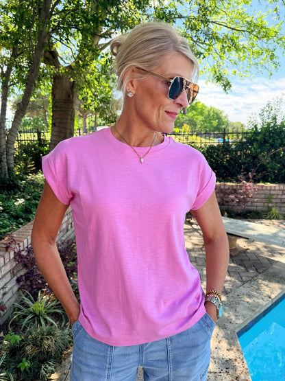 Woman wearing a pink  short sleeve, elevated tee shirt and sunglasses outdoors by a pool