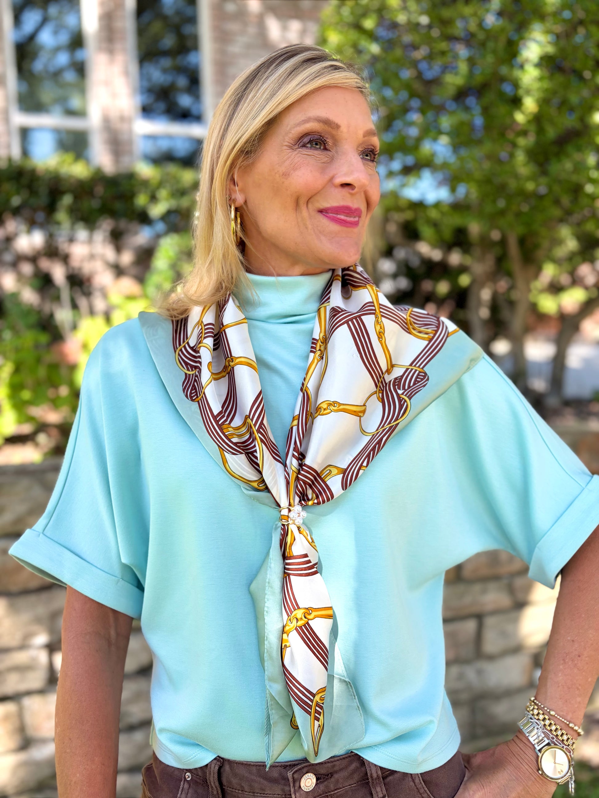 woman in a seafoam colored modal mock neck top that is short sleeved paired with a horsebit scarf.