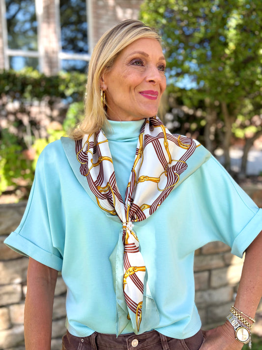 woman in a seafoam colored modal mock neck top that is short sleeved paired with a horsebit scarf.