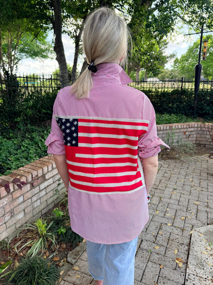 woman wearing a red and white pinstripe, long sleeve oxford with the american flag on the back. 
