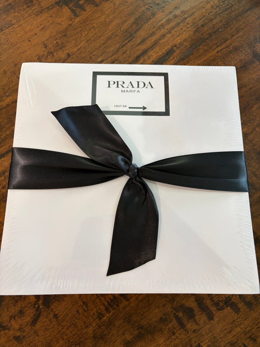 white note pad that says PRADA MARFA and is wrapped in black ribbon