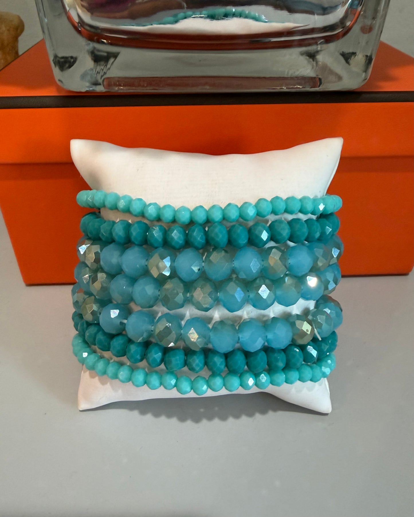 Stack of turquoise beaded bracelets on a white pillow with an orange box in the background