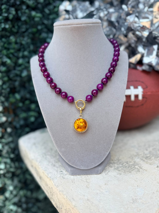 A beaded necklace with deep purple beads and a gold-tone ring connector holding a round amber-yellow pendant.
