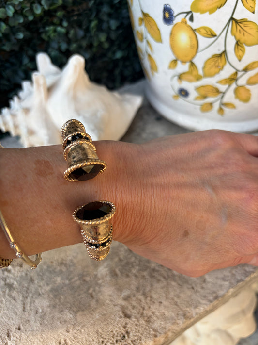 large gold bangle elevated with black gemstones on end and beaded gold detail