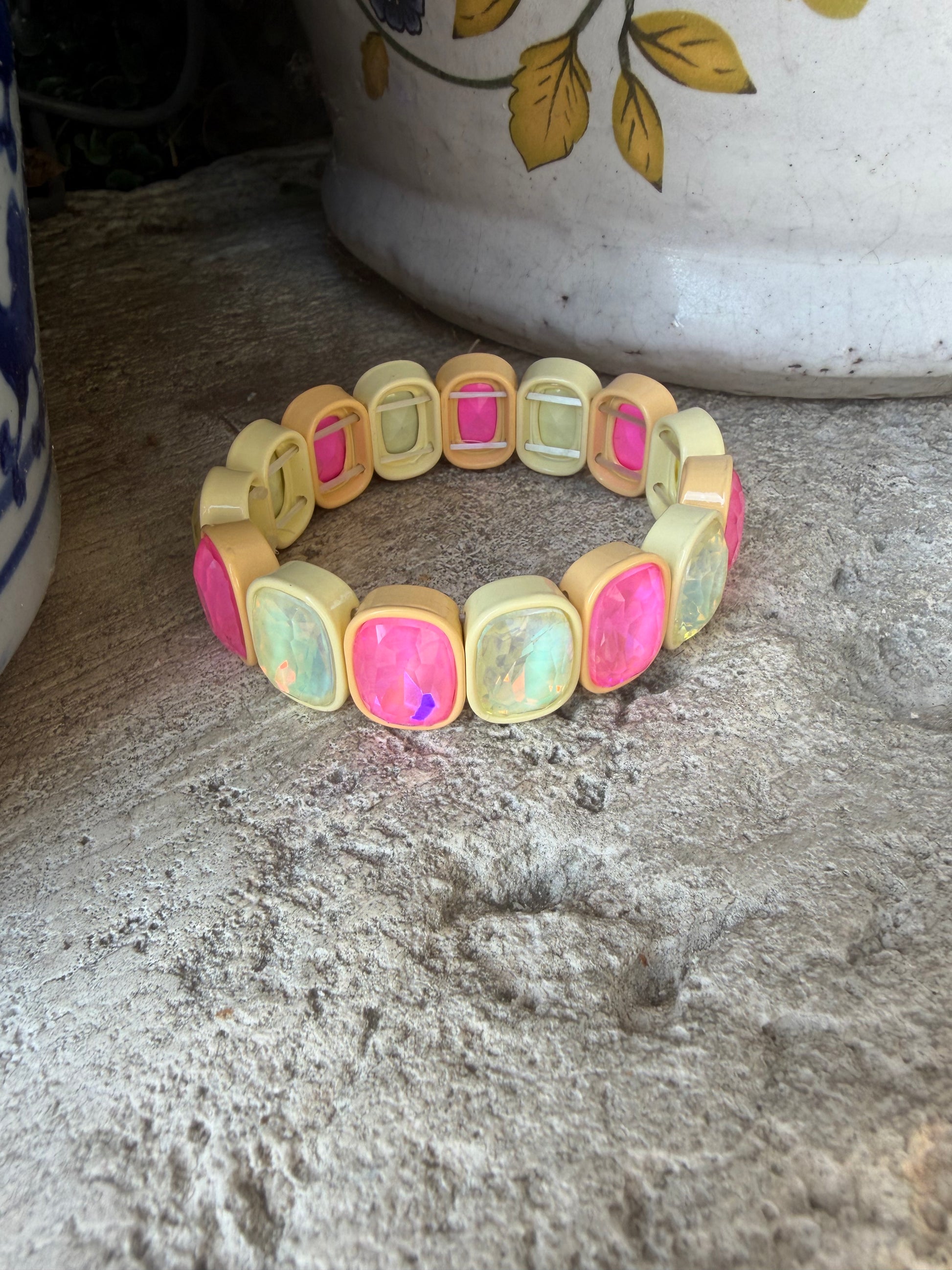 A beaded stretch bracelet featuring iridescent pink and light butter colored stones set in a pale yellow resin, displayed on a textured gray stone surface.