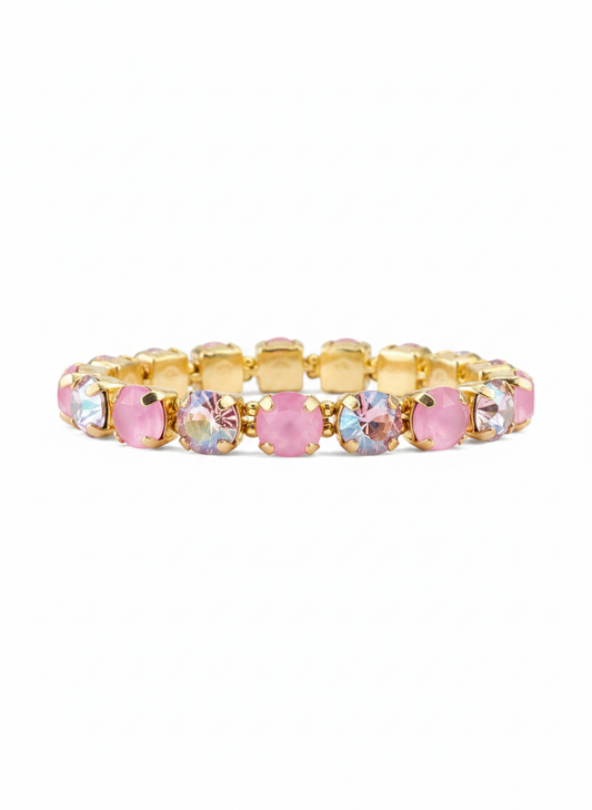 A gold-plated tennis bracelet featuring alternating round pink faceted crystals and oval iridescent clear crystals, displayed against a solid white background.