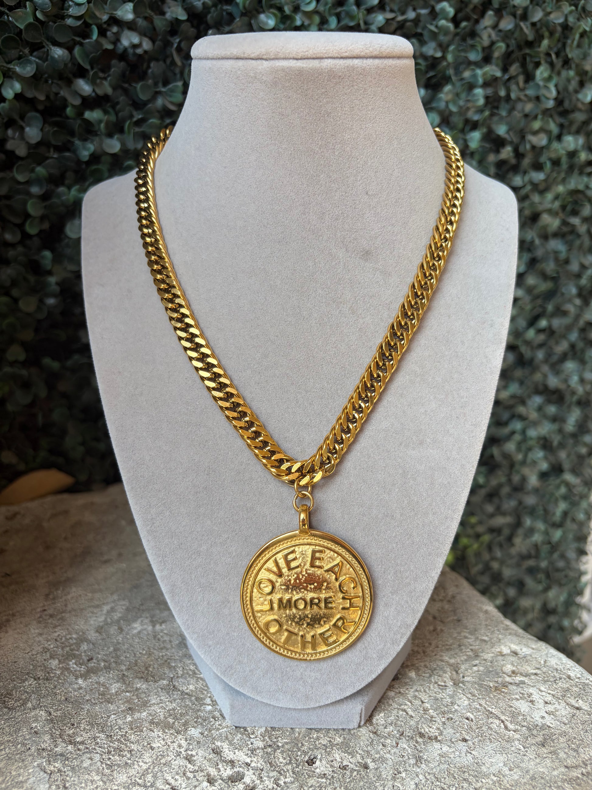 A rich gold tone, water resistant, non tarnish medallion necklace that says "love each other more" . gold link and adjustable
