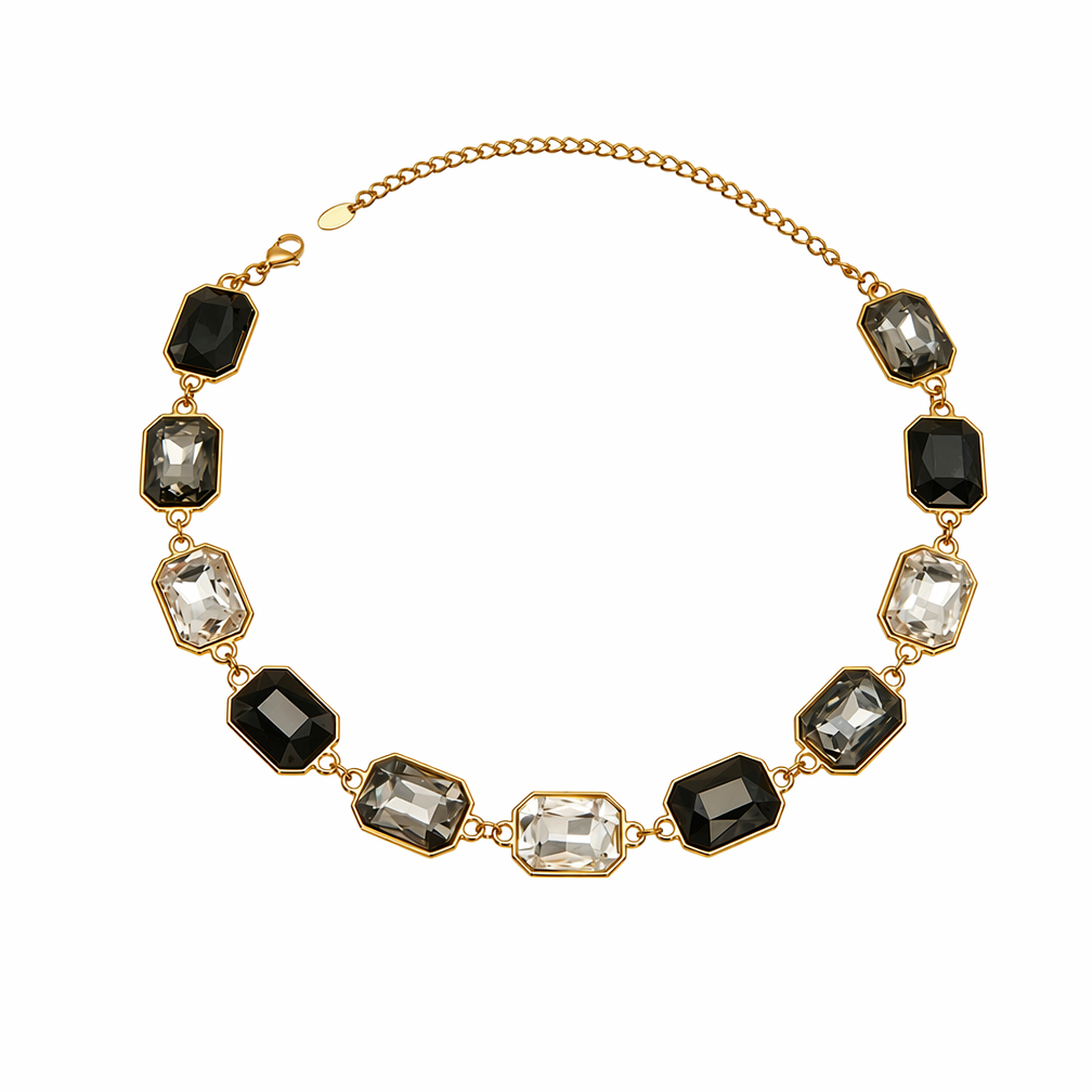 A gold-tone chain necklace featuring a row of rectangular faceted gemstones in black, smoky gray, and clear, arranged in an oval pattern on a white background.